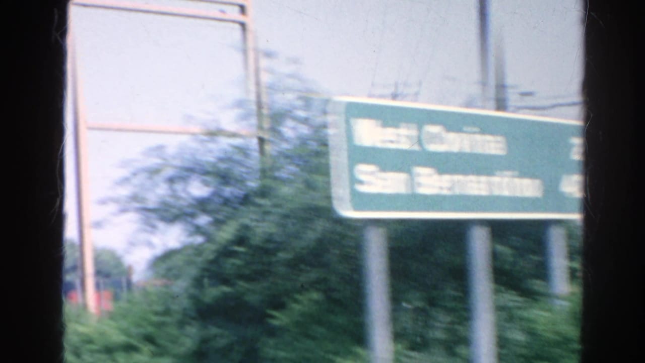 Green freeway sign beside a highway seen from inside a moving car.