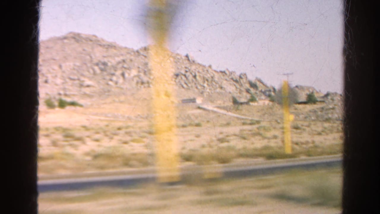 Blurred roadside markers pass in front of rocky desert hills.