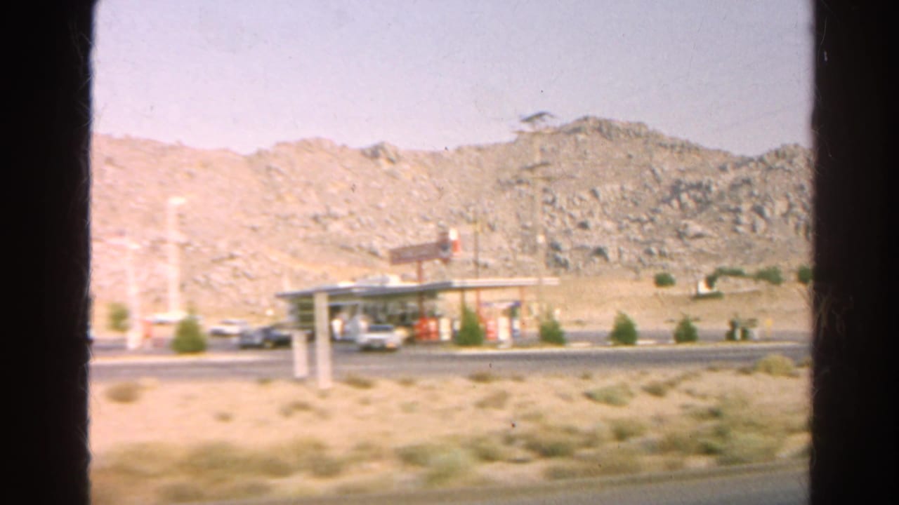 Roadside gas-station canopy near rocky hills and parked cars.