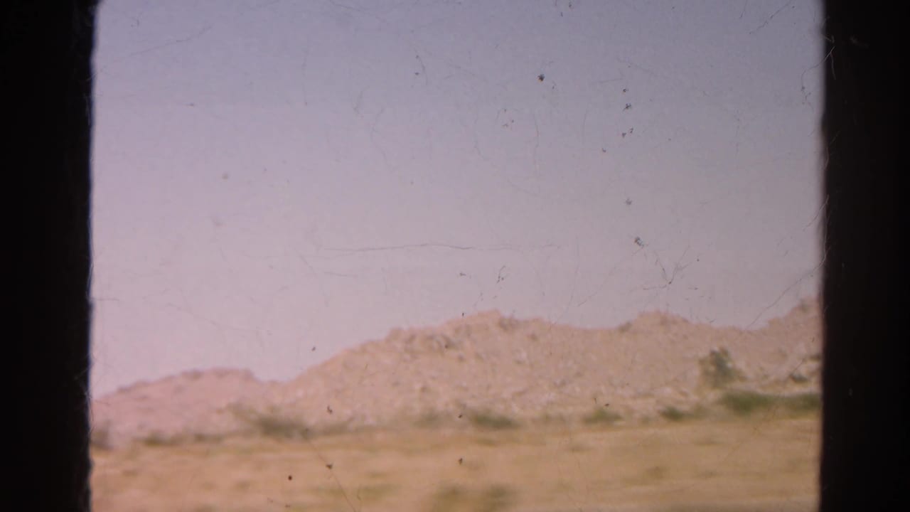 Arid roadside and low rocky hills seen through dark vertical film-frame borders.