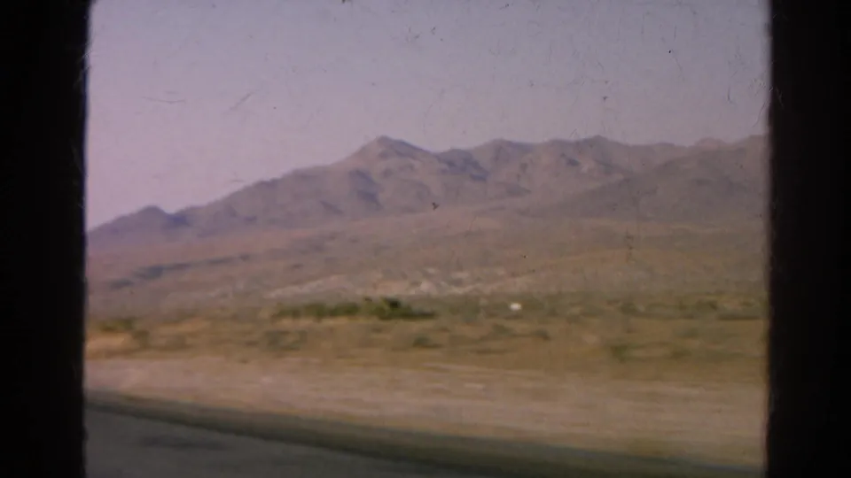 1966 8mm view near Silver Lake, California, with a dry road shoulder, scattered scrub, mountain ridge, and visible film scan borders.