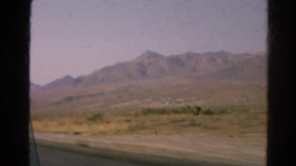 1966 8mm road-trip view from inside a moving car, showing desert terrain and distant mountains.