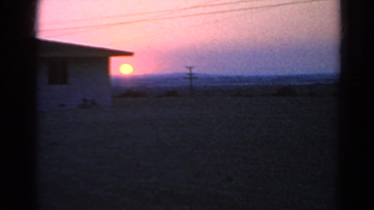 Low sun beside a white house, with power lines and dark window framing over open land.