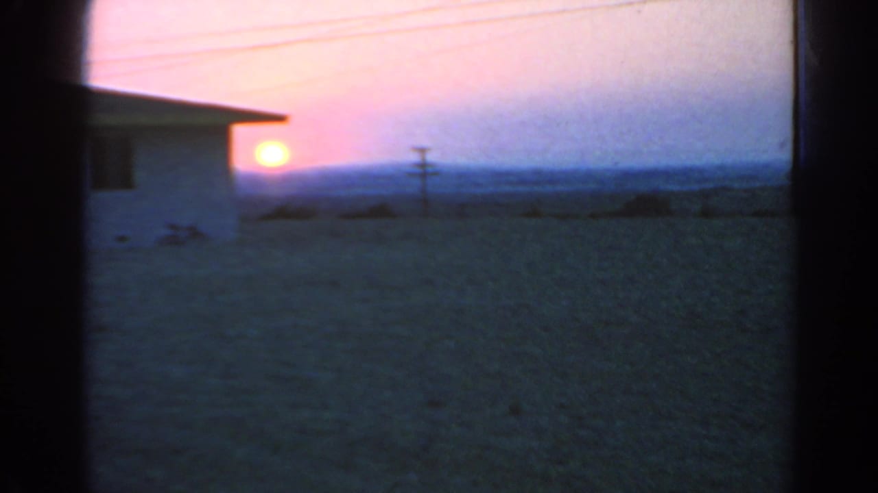Sunset over open ground with a building edge and utility pole in silhouette.