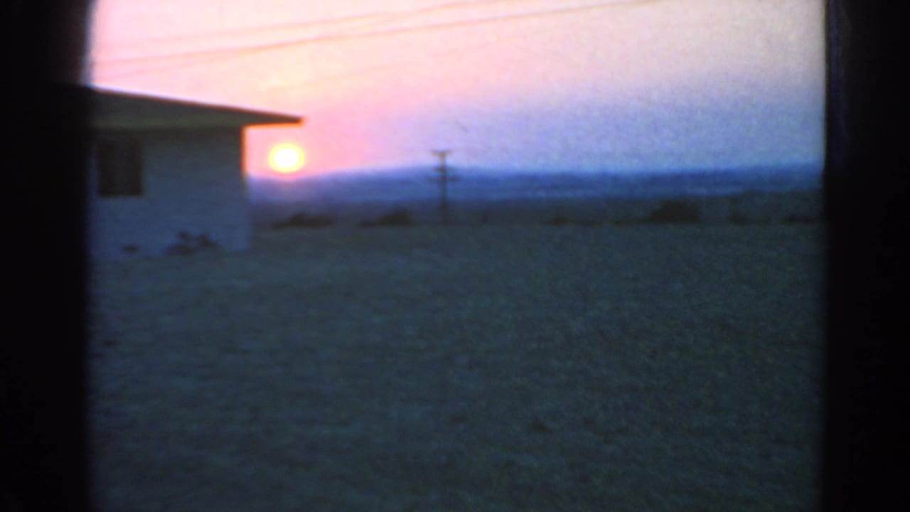 Low sun at dusk beside a dark building edge, with open ground and a utility pole.