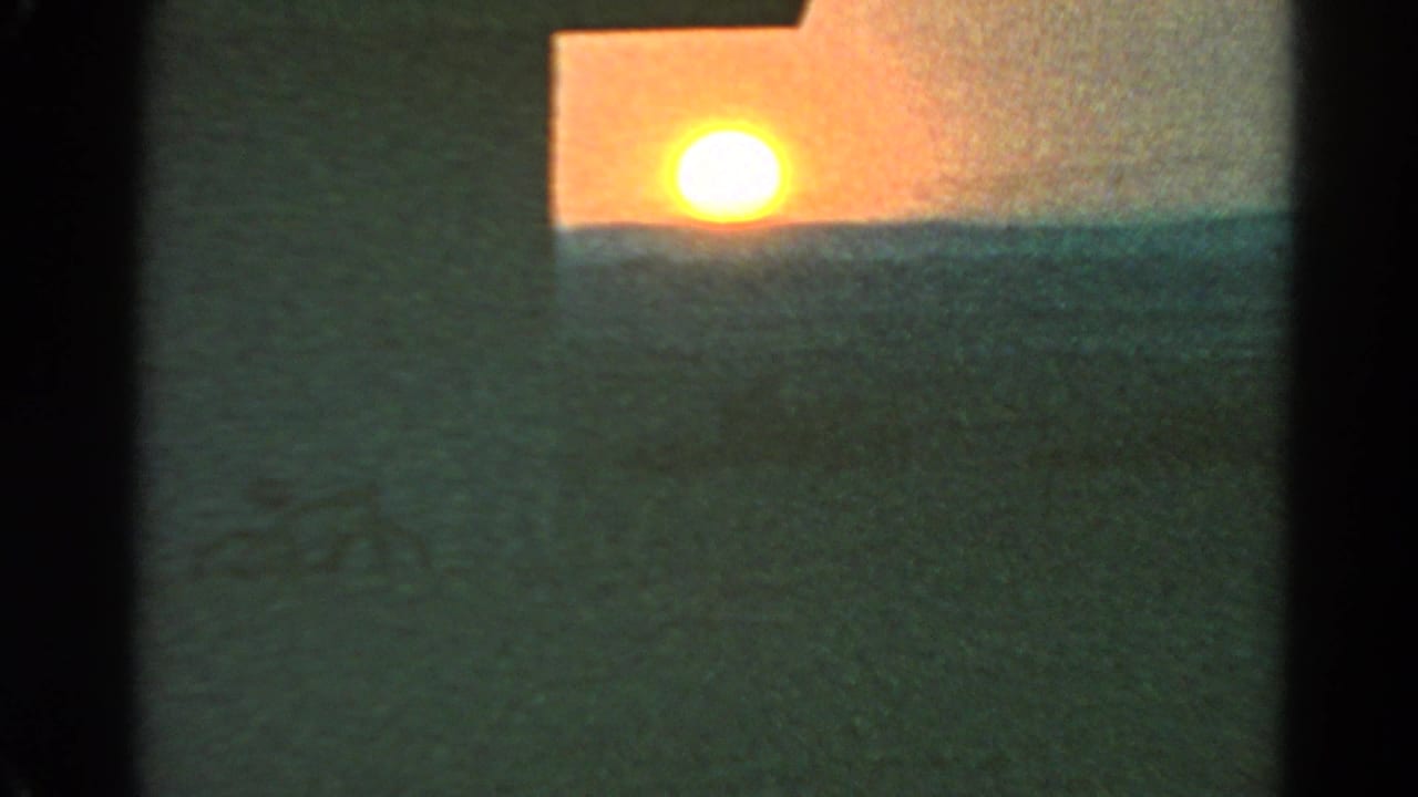 1966 8mm Silver Lake frame with a blown-out sun at the horizon, a dark roofline, soft grain, and shadowed open ground.