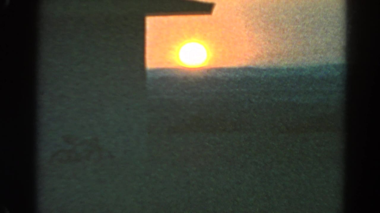 1966 Silver Lake 8mm frame showing the sun low against an orange sky, with a dark building wall and open ground in front.