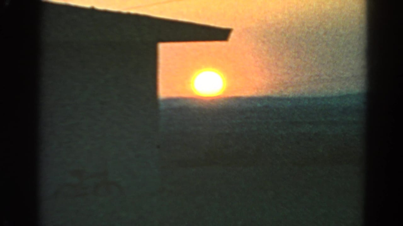 Low sun near a distant horizon beside a dark building silhouette.