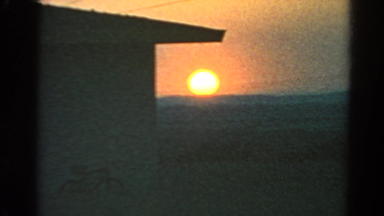 1966 Silver Lake home-movie frame with the glowing sun above a dark hillside horizon and a building edge in silhouette.