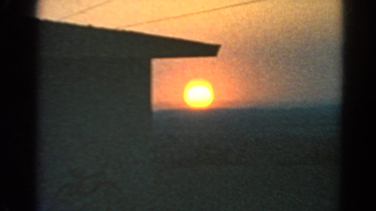 1966 Silver Lake 8mm frame showing the sun dropping toward a dim horizon, with faint overhead lines and a dark structure in front.