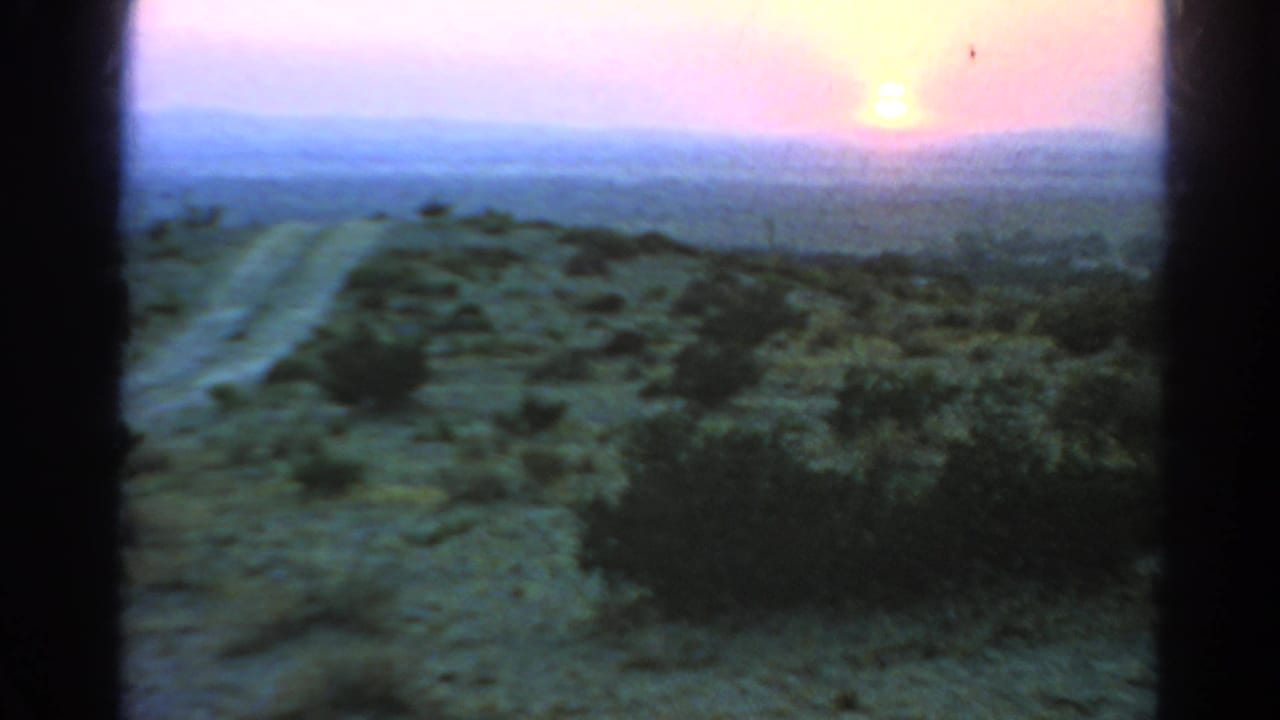 1966 Silver Lake 8mm frame looking toward a hazy sunset over scrubland, a dirt road, and distant hills.
