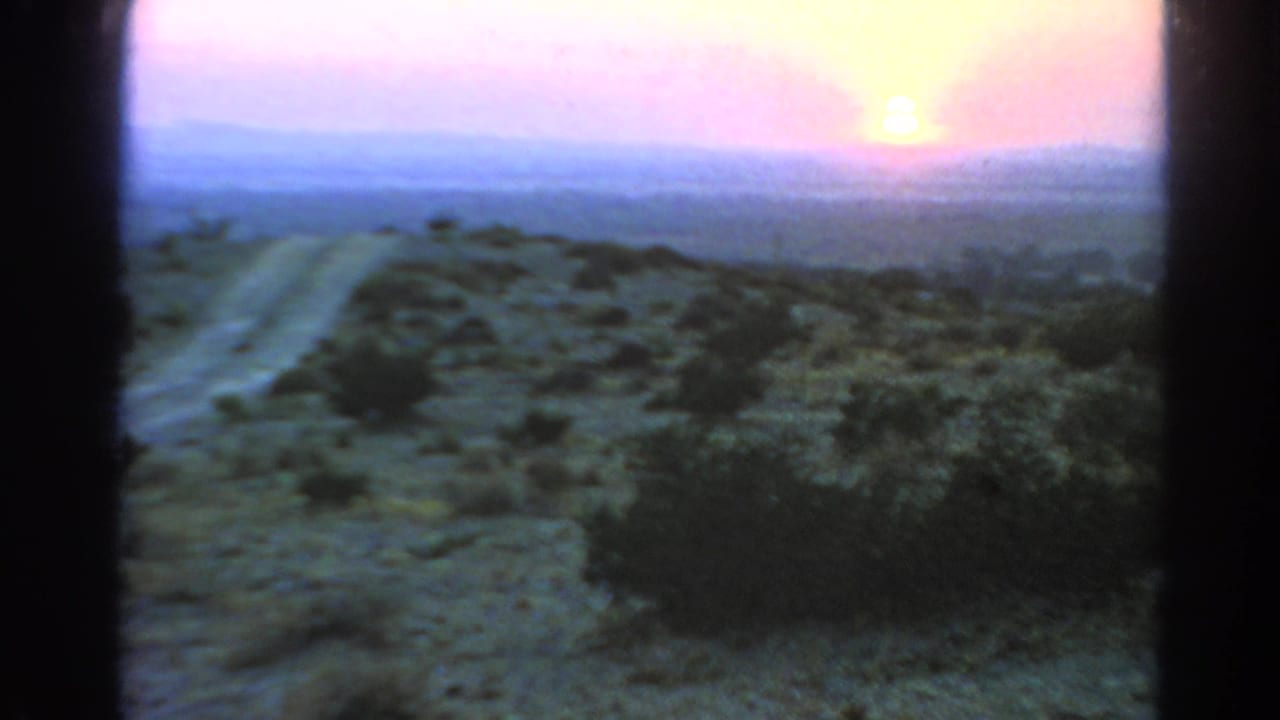 Low sun over scrubby desert terrain with a dirt road and dark 8mm frame borders.