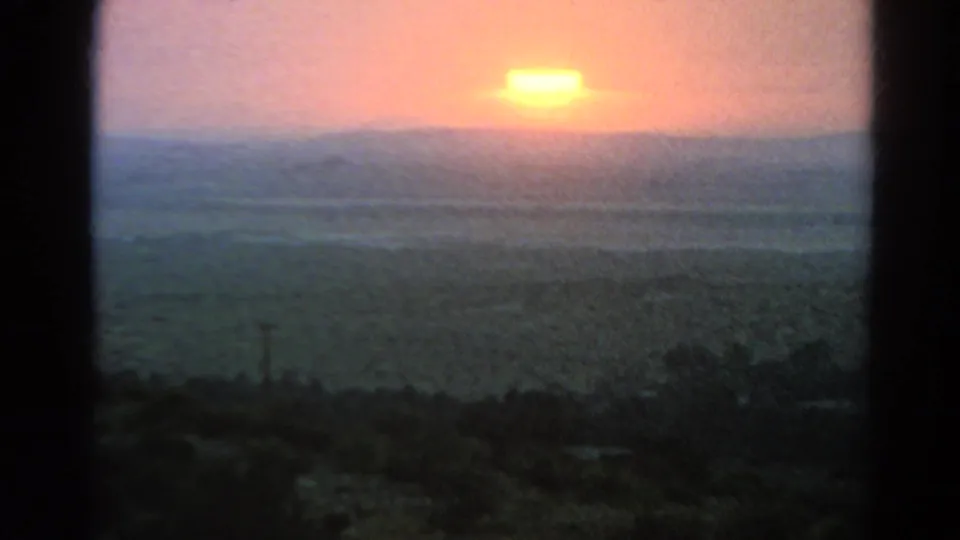 The 8mm frame centers on the orange sun over a hazy arid horizon, with dark scrub and soft color shifts across the lower frame.
