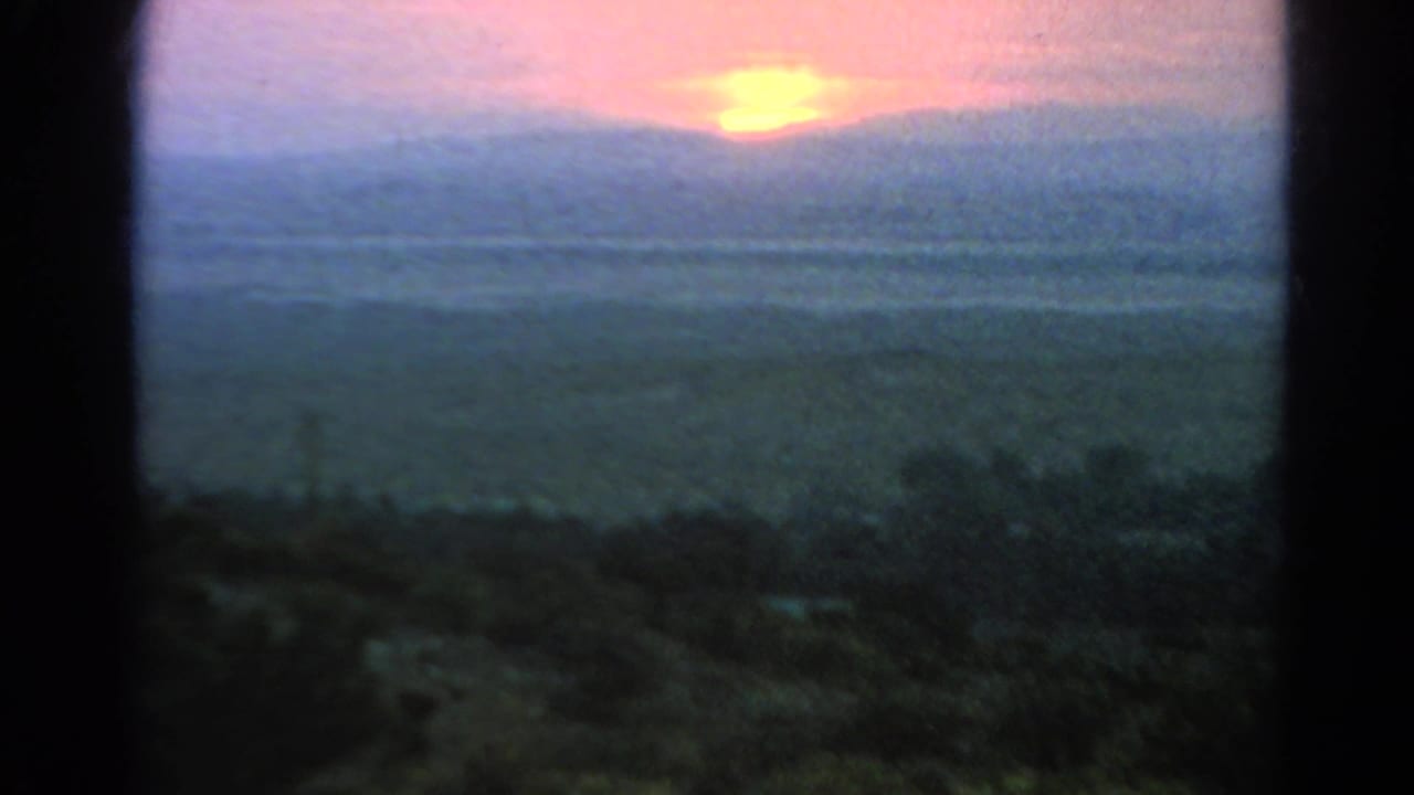 1966 Silver Lake home-movie frame showing a soft pink sun above distant hills, partly bordered by a dark window or doorway.