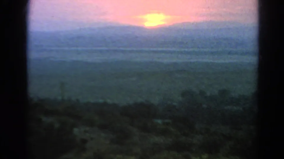 1966 Silver Lake home-movie frame showing a soft pink sun above distant hills, partly bordered by a dark window or doorway.