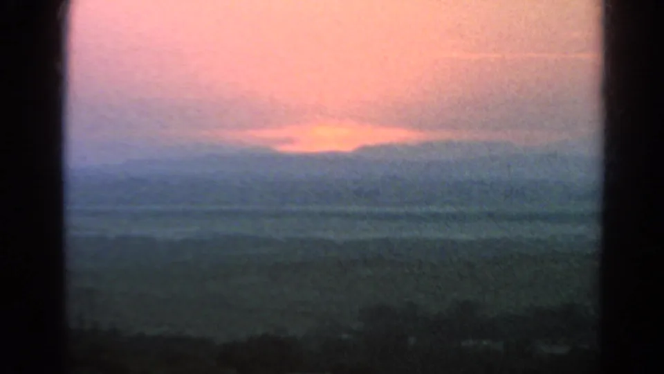 1966 Silver Lake sunset view with the sun dropping behind a cloud bank and distant hills, bordered by dark foreground framing.