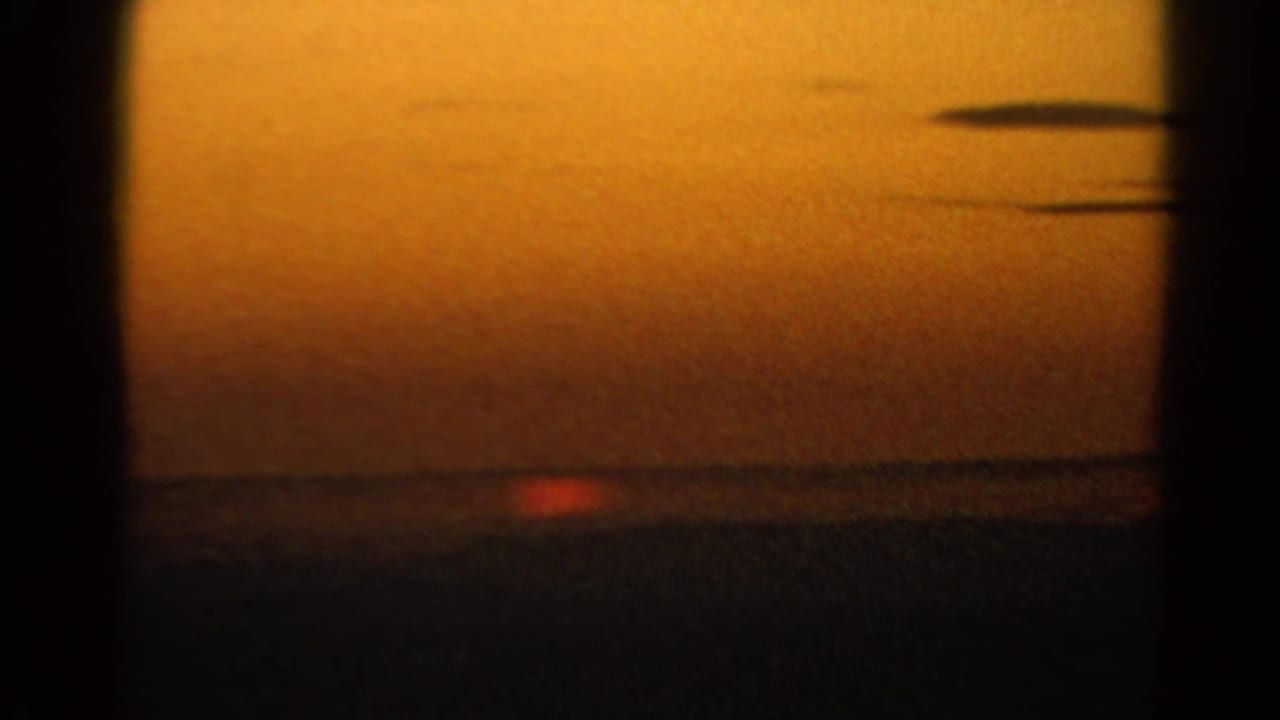 1966 Silver Lake home-movie frame showing a red-orange sun near the horizon under a warm sky and dark cloud streaks.