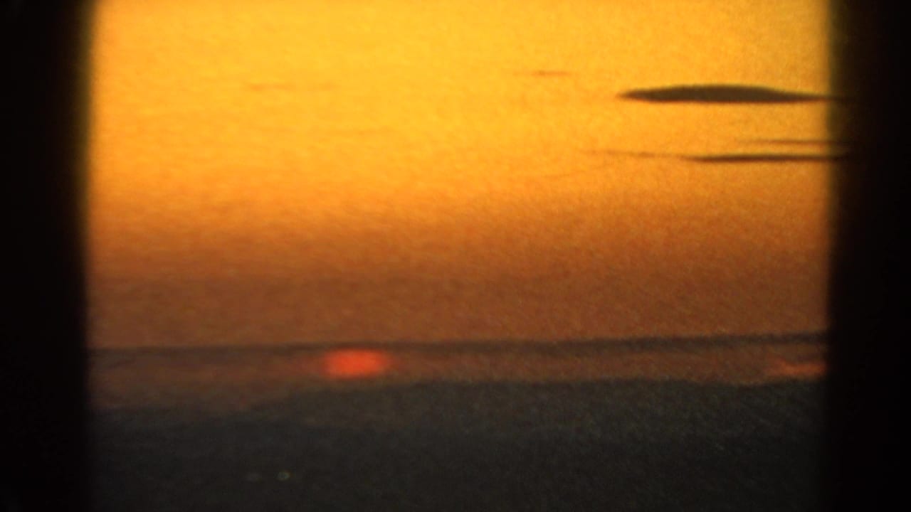 Low orange sun at the horizon over dark water, with heavy film grain and vertical edge shadows.