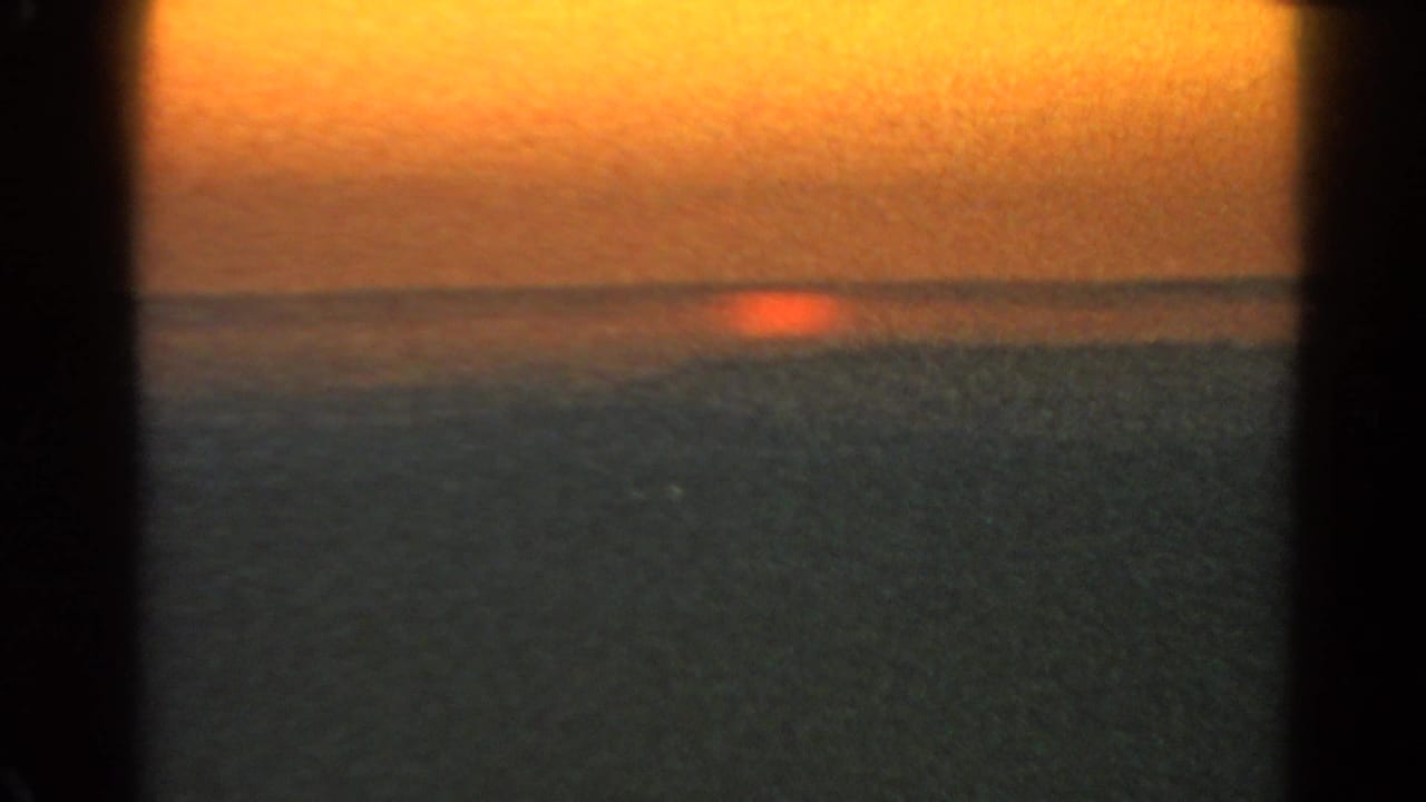 1966 Silver Lake sunset frame with a small red sun sinking toward the horizon over dark water and a warm sky.