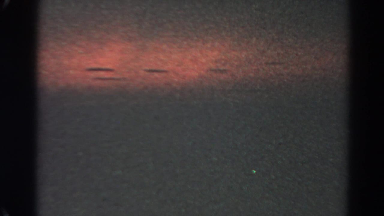 1966 Silver Lake night-sky frame with a broad red glow, faint colored points, dark borders, and pronounced 8mm grain.