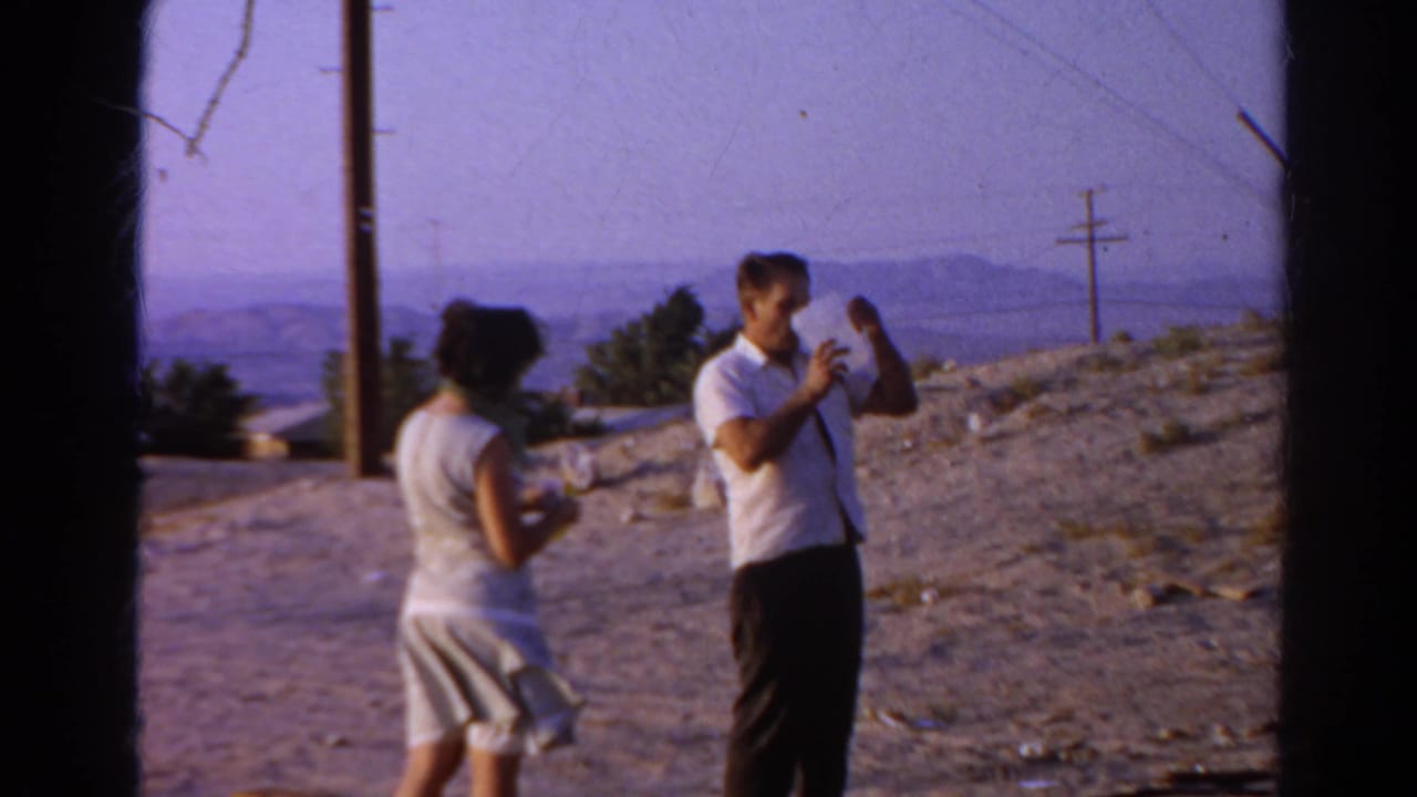 In the Silver Lake 1966 scene, the man raises or inspects the pitcher as the woman stands nearby against utility poles and distant hills.