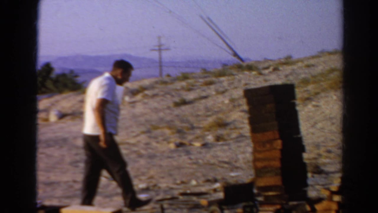 Man walks past a brick stack on a dusty slope with a white cup nearby.