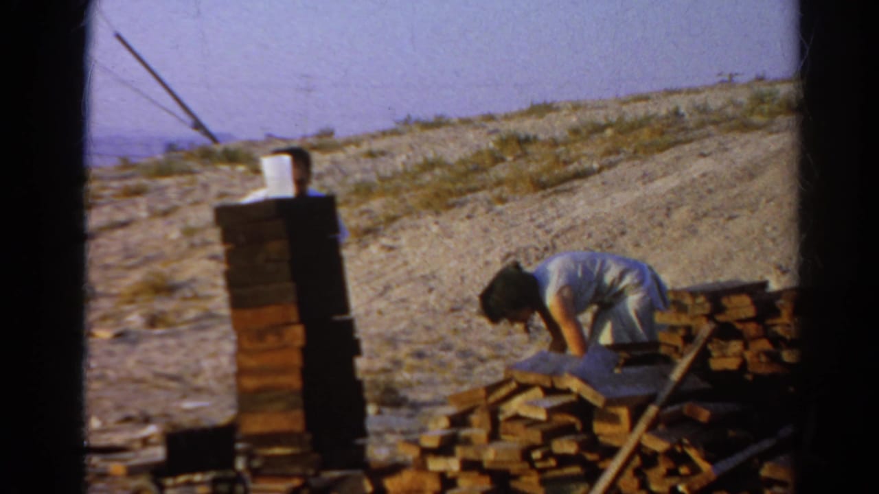 1966 Silver Lake frame with a woman bending near boards and a partly visible man behind stacked lumber.