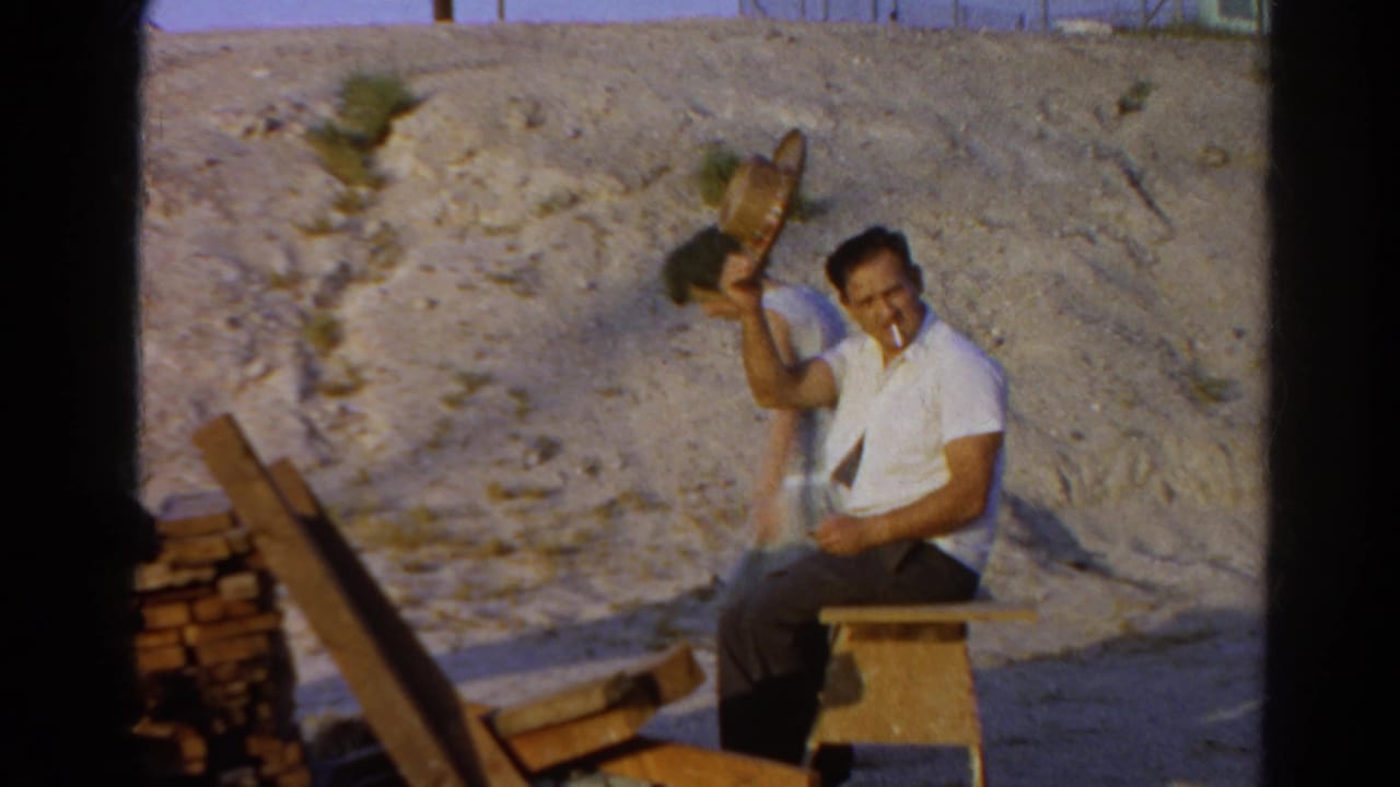 The seated man lifts his straw hat and appears to hold a cigarette in his mouth at the Silver Lake outdoor work area.
