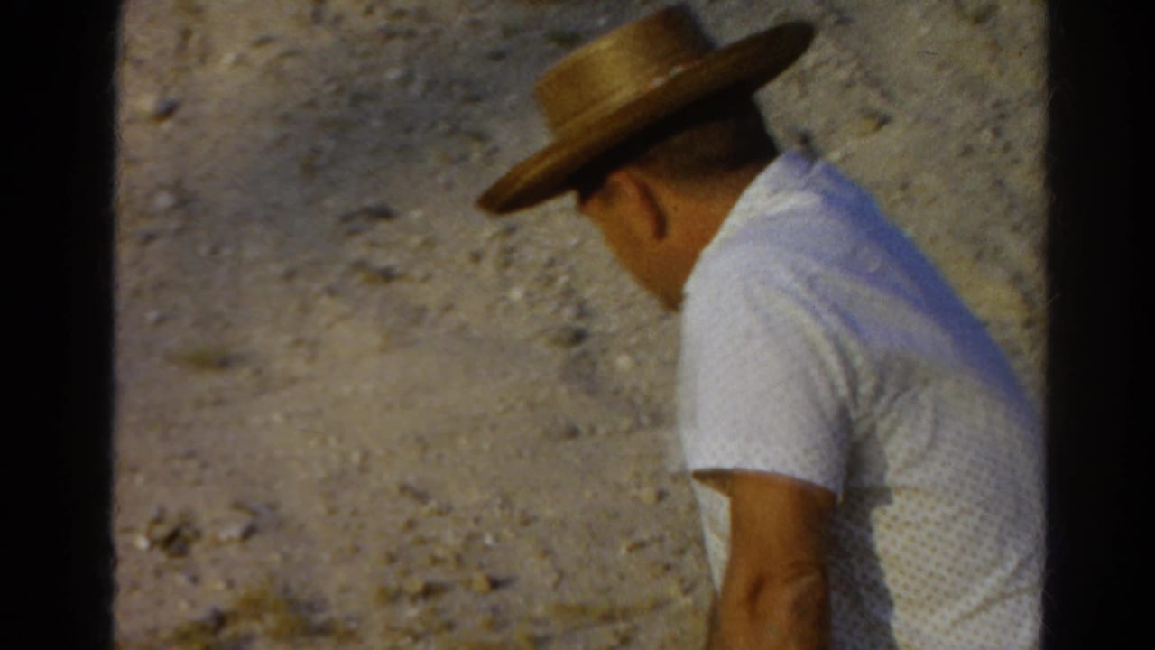 1966 Silver Lake frame showing the man turned away, his straw hat and white shirt silhouetted against the dry slope.