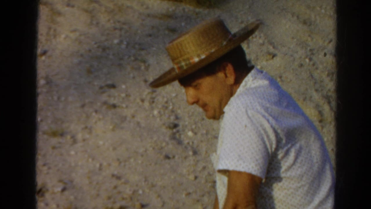 In 1966 Silver Lake home-movie footage, a seated man in a straw hat and white patterned shirt looks down on a gravel surface.