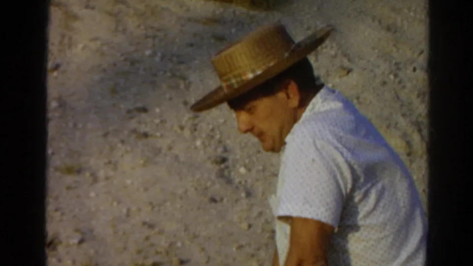 In 1966 Silver Lake home-movie footage, a seated man in a straw hat and white patterned shirt looks down on a gravel surface.