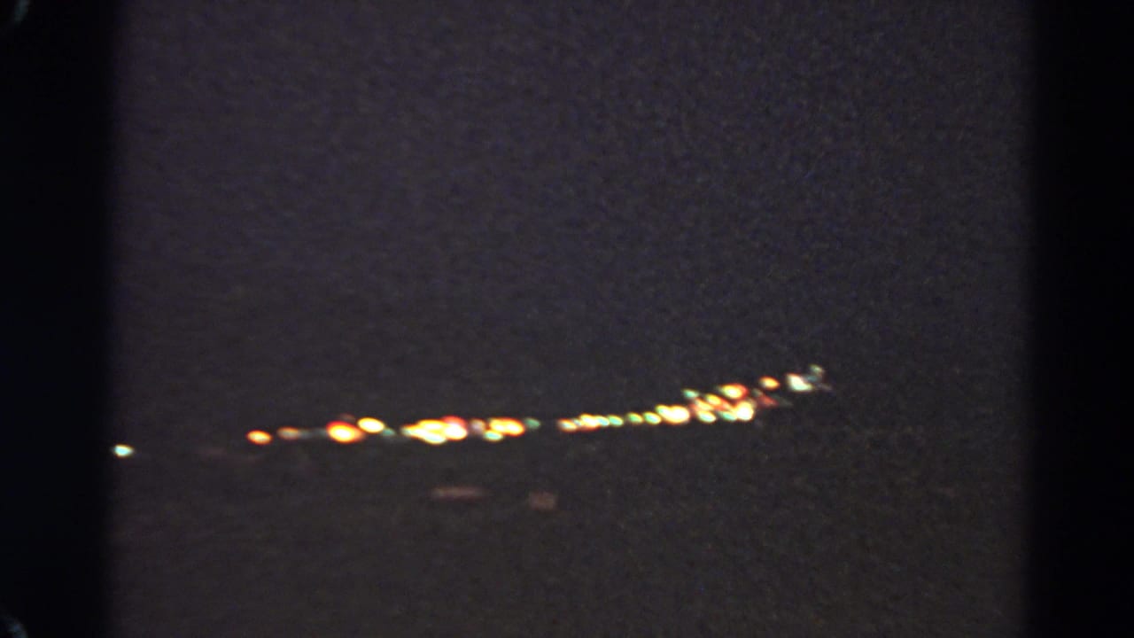 1966 8mm frame from Silver Lake showing a low band of distant city lights in soft focus at night.