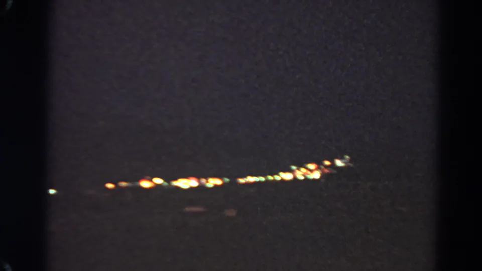 1966 8mm frame from Silver Lake showing a low band of distant city lights in soft focus at night.