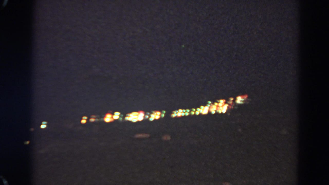 Dark 8mm frame with scattered distant lights, likely an adjacent travel shot from the same home-movie clip sequence.