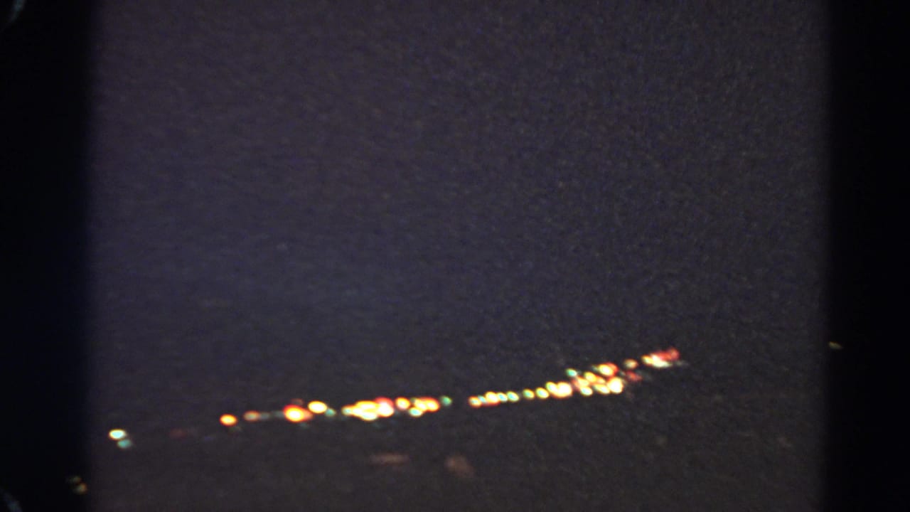 Dark frame with distant lights and heavy film grain.