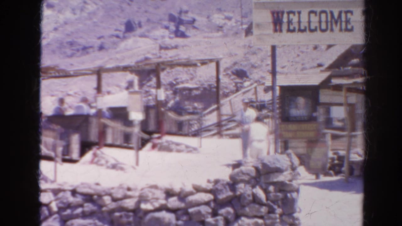 Visitors near open ride carts beneath a Welcome sign at a rocky attraction.
