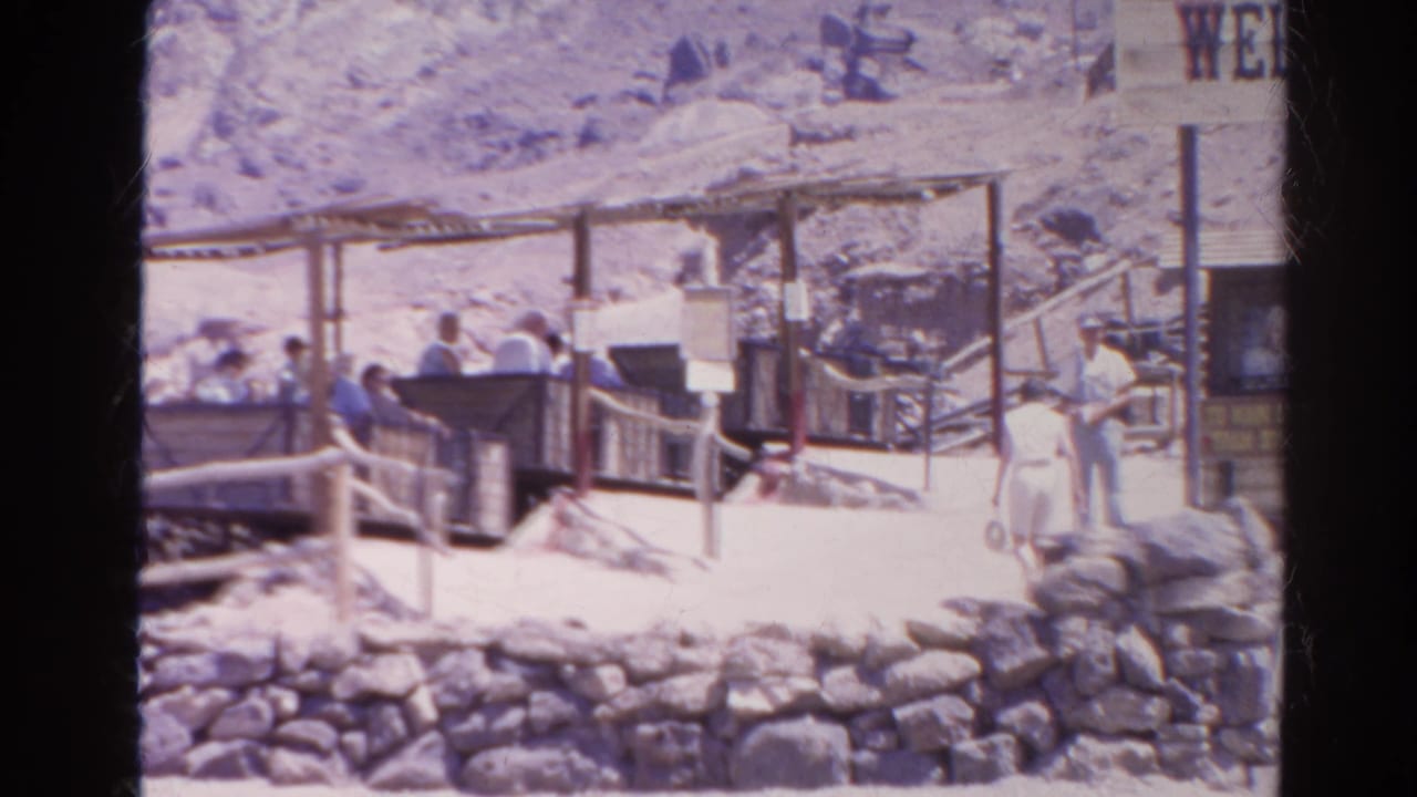 1966 Silver Lake, California frame with visitors in light clothing near open carts, narrow track structures, and a rocky hillside.