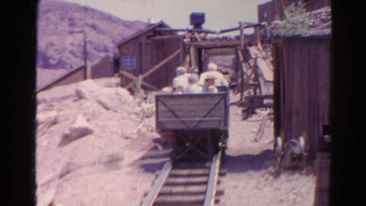 A mine cart with several men sits on rails between rough wooden structures.