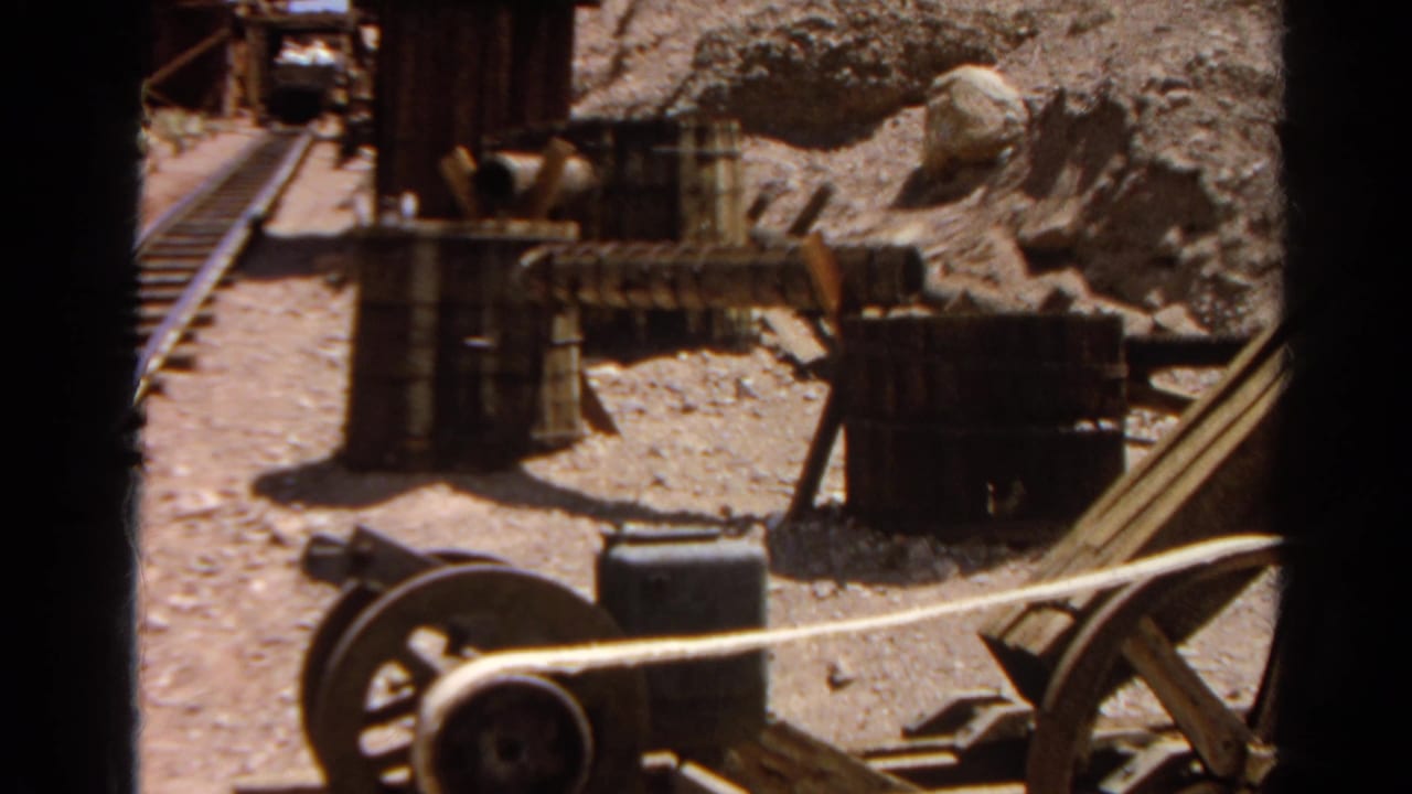1966 8mm frame showing mining-site equipment, barrels, rails, and rocky dry terrain at Silver Lake, California.
