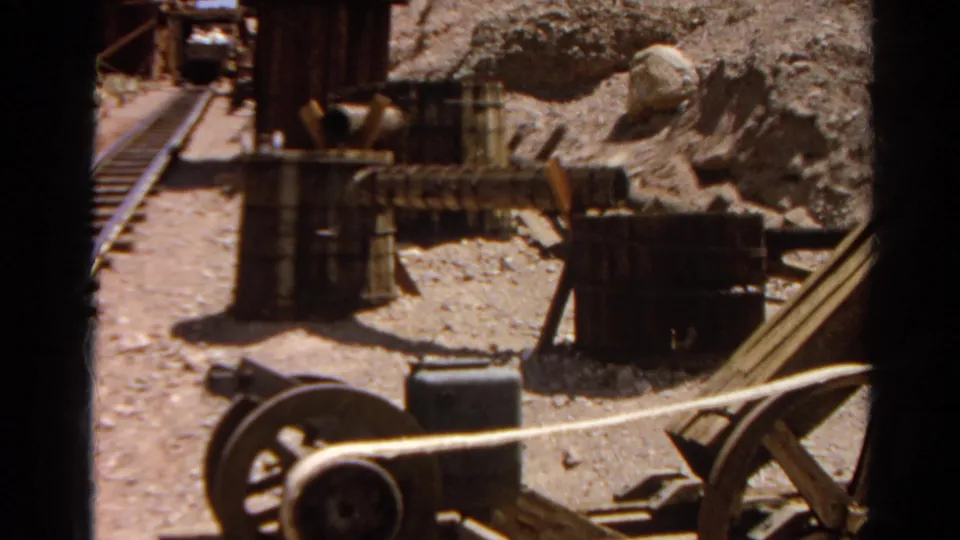 1966 8mm frame showing mining-site equipment, barrels, rails, and rocky dry terrain at Silver Lake, California.