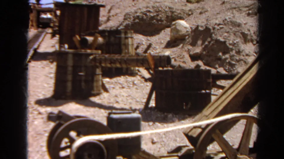 1966 Silver Lake home-movie frame of a sunlit rocky industrial site with barrels, wooden bins, and a large wheel.