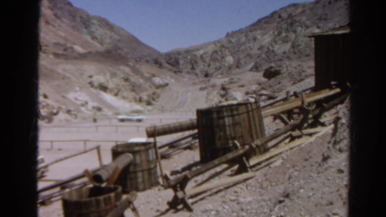 1966 Silver Lake frame showing a rocky desert road, distant vehicle, and foreground pipes and wooden equipment.