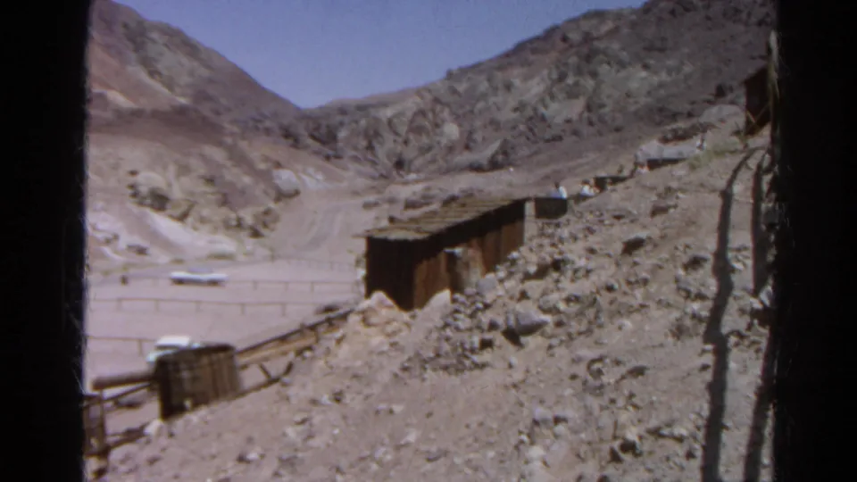 1966 Silver Lake, California frame with a shed-like mining structure, rails, rubble, fencing, mountains, and a white car below.
