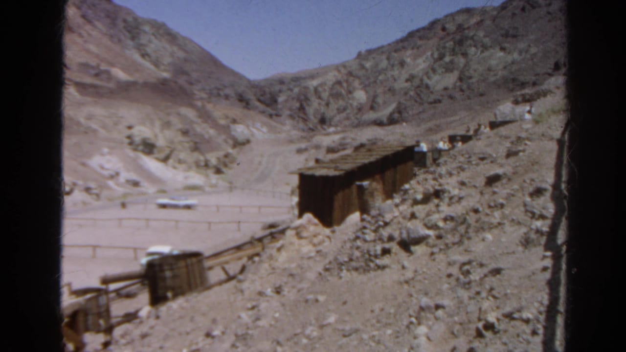 1966 Silver Lake, California 8mm frame showing a mining shed, rubble slope, fence, distant car, and arid mountain terrain.