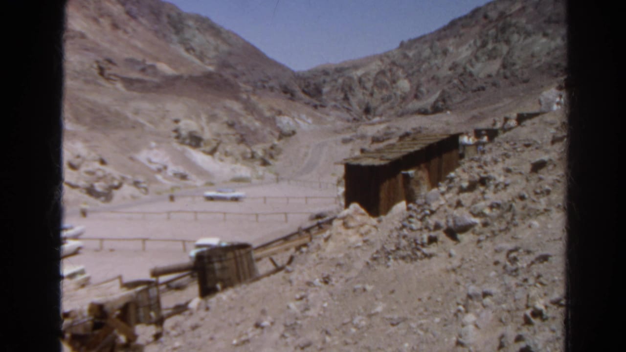 1966 Silver Lake, California frame with rails, ore carts or bins, a shed-like structure, rubble, fencing, and mountains beyond.