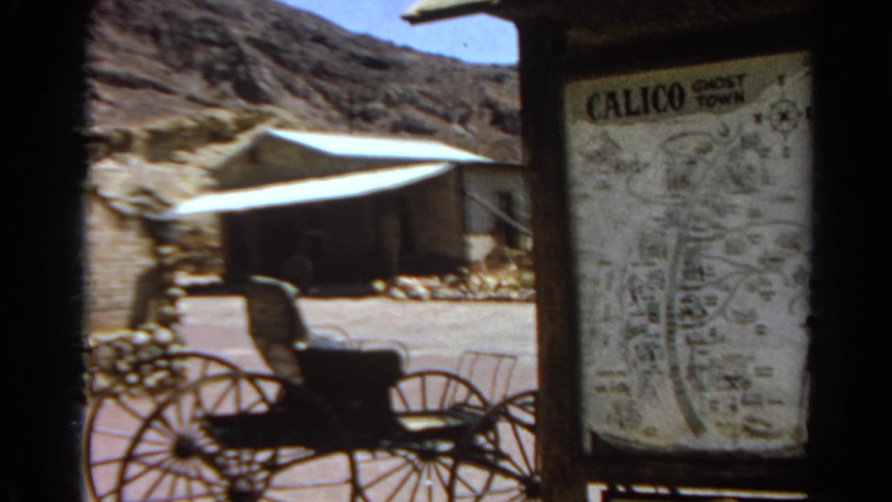 Horse-drawn carriage in front of a Calico Ghost Town map sign and desert buildings.