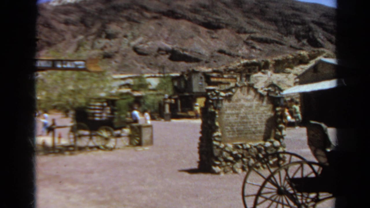 Western-themed town street with stagecoach, stone sign, visitors, and rocky hillside.