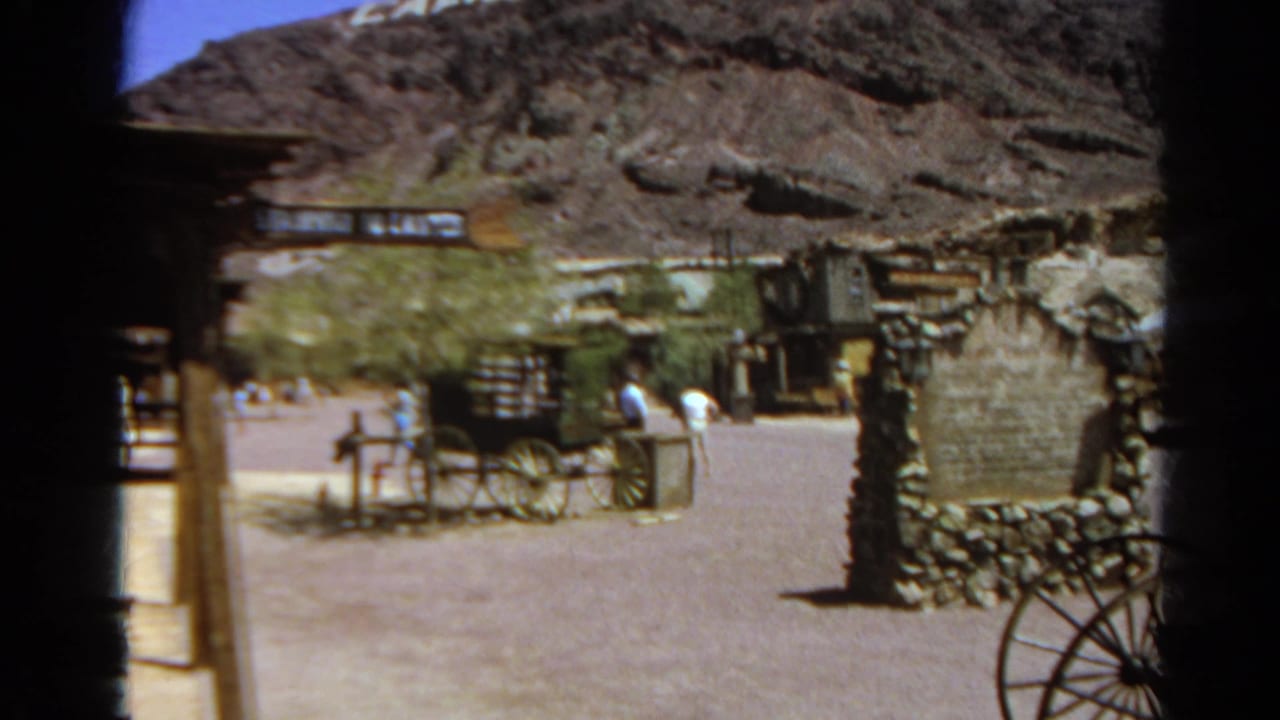 Visitors pass through a sunlit Western-themed town in Silver Lake, California, with a wagon display and rustic structures visible.