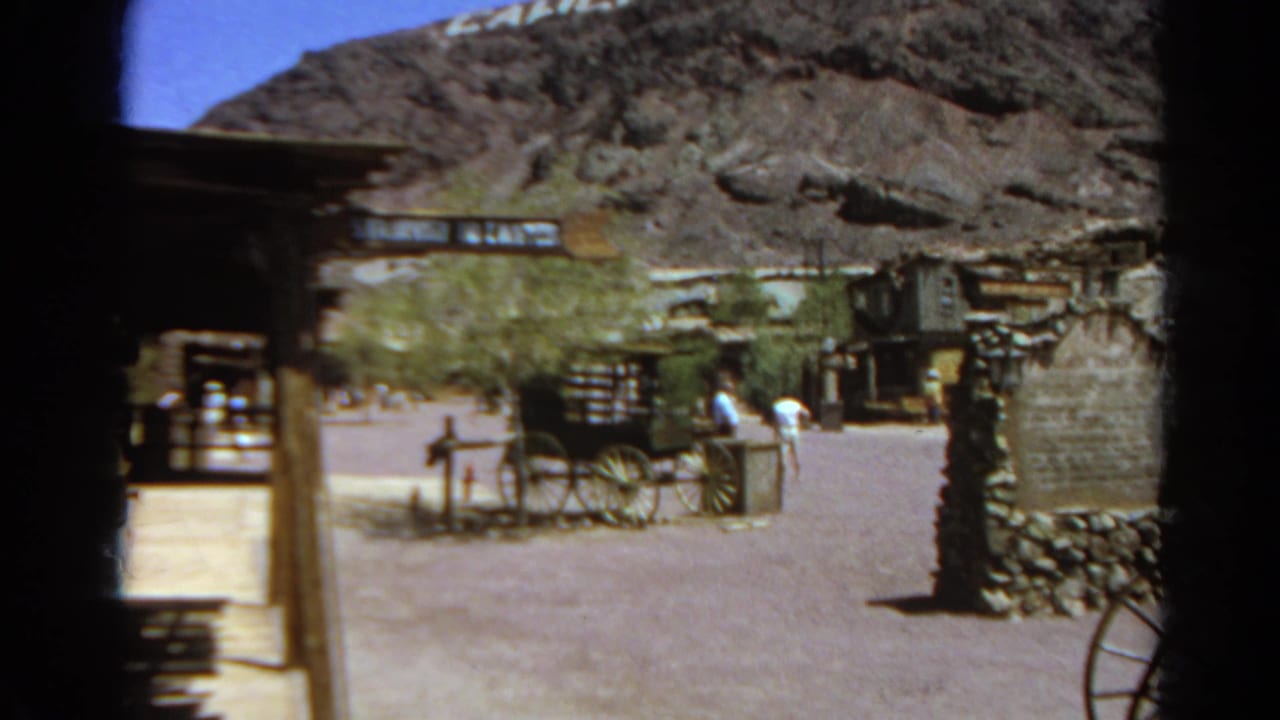 A handheld 1966 home-movie view shows visitors walking near a wagon display and Western-style structures at Silver Lake, California.
