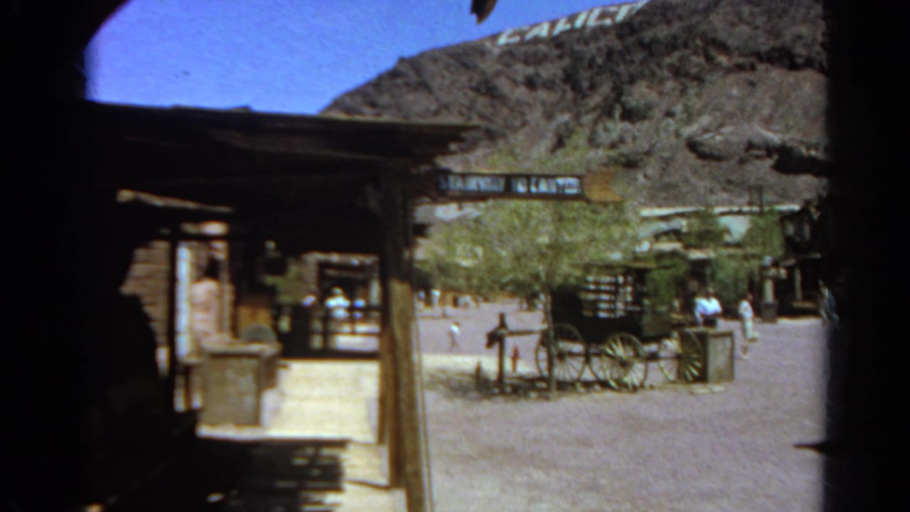 Rustic outdoor courtyard with wagon, trees, wooden structures, and a partial hillside sign.